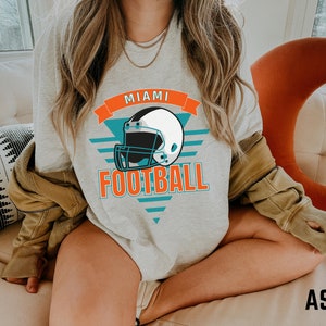 May include: A gray sweatshirt with a graphic of a football helmet and the text "Miami Football" in orange and teal.