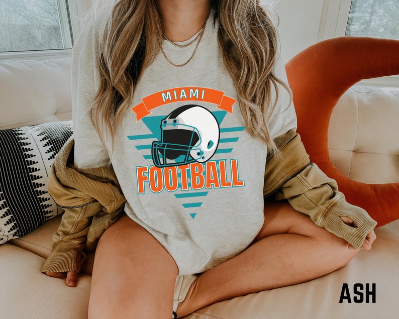 May include: A gray sweatshirt with a graphic of a football helmet and the text "Miami Football" in orange and teal.