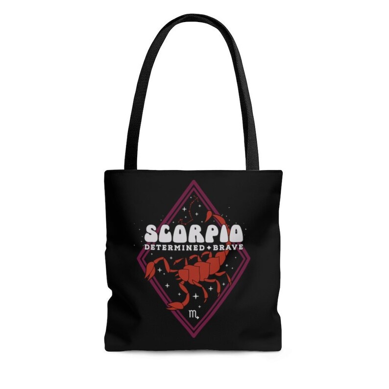 May include: Black tote bag with black handles. The bag features a red and white graphic of the Scorpio zodiac sign, with the words "SCORPIO DETERMINED + BRAVE" in white text. The design is set within a purple diamond.