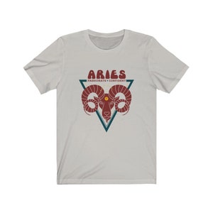 May include: A light gray t-shirt with a red and blue graphic of an Aries zodiac sign. The graphic includes the text "Aries" in a retro font and "Passionate - Confident" in a smaller font.