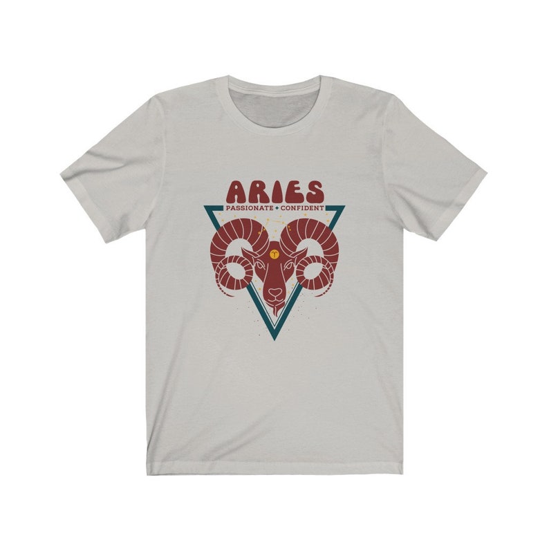 May include: A light gray t-shirt with a red and blue graphic of an Aries zodiac sign. The graphic includes the text "Aries" in a retro font and "Passionate - Confident" in a smaller font.