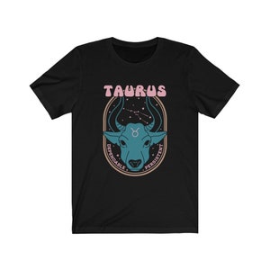 K&ouml;nnte beinhalten: Schwarzes T-Shirt mit einem Grafikdruck eines blauen Bullenkopfes vor einem Hintergrund aus Sternenbildern. Der Text "TAURUS" befindet sich &uuml;ber dem Bullenkopf und die W&ouml;rter "DEPENDABLE" und "PERSISTENT" befinden sich auf beiden Seiten des Bullenkopfes.