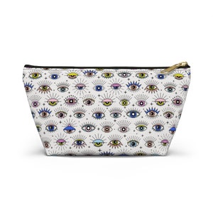 Puede incluir: Bolsa blanca con cremallera con un patrón repetido de ojos coloridos con pestañas y rayos de luz.