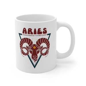 May include: White ceramic mug with a red and blue illustration of an Aries zodiac sign. The text "Aries" is in a retro font and the words "Passionate + Confident" are below the sign.