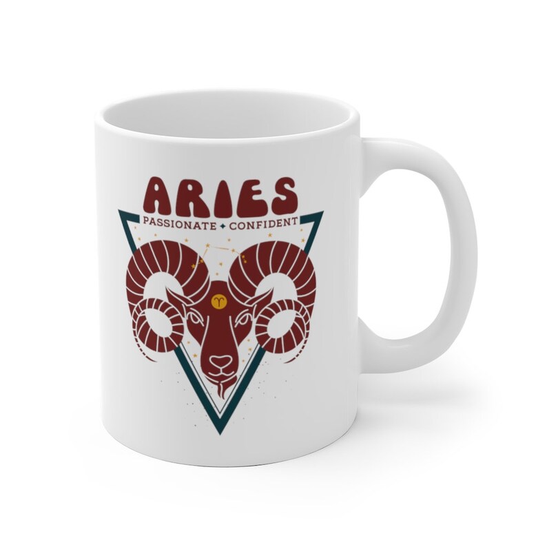May include: White ceramic mug with a red and blue illustration of an Aries zodiac sign. The text "Aries" is in a retro font and the words "Passionate + Confident" are below the sign.