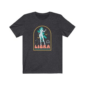 Może przedstawiać: Szary t-shirt z nadrukiem przedstawiającym kobietę trzymającą wagę, z tekstem "LIBRA CHARMING &bull; DIPLOMATIC" poniżej.