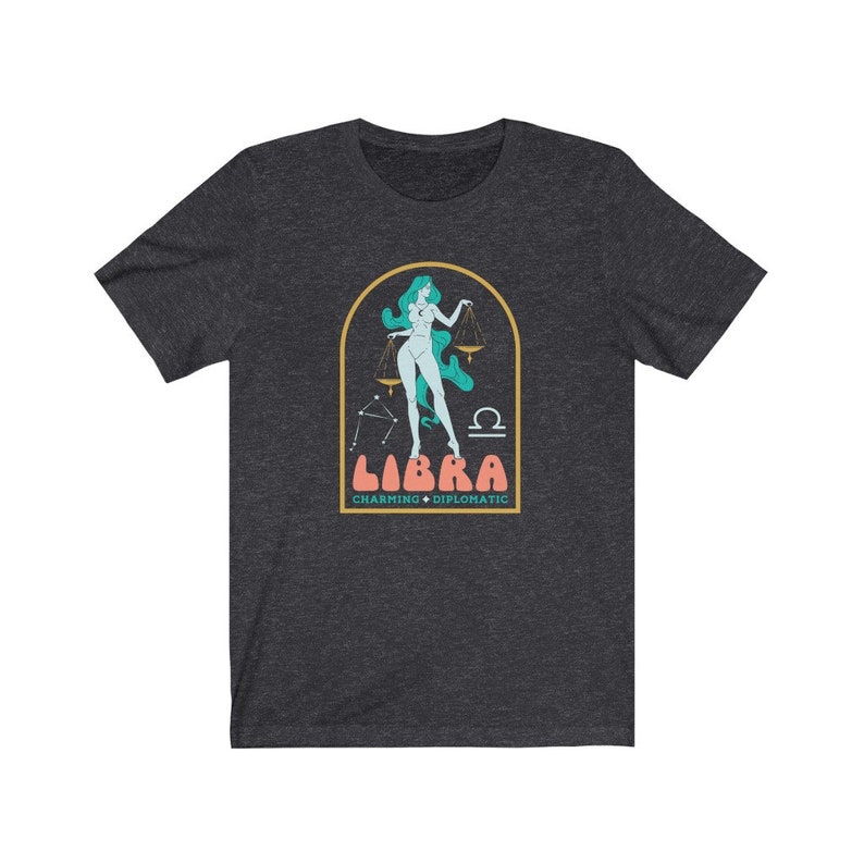 Może przedstawiać: Szary t-shirt z nadrukiem przedstawiającym kobietę trzymającą wagę, z tekstem "LIBRA CHARMING &bull; DIPLOMATIC" poniżej.