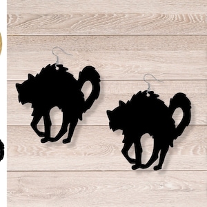 Puede incluir: Pendientes de gato negro en silueta. El gato está en posición de cuclillas con la cola enroscada. Los pendientes están hechos de un material negro y tienen un gancho plateado.