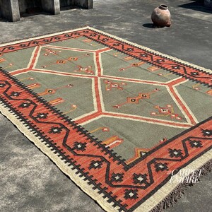Handwoven Moroccan kilim rug in sage green with terracotta diamond medallions tribal motifs and multi band zigzag border. Wool jute flatweave. Custom area rug sizes India.