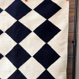 Minimalist wool rug featuring a timeless black and white diamond grid. The handwoven construction ensures quality and durability, while the 100% wool composition creates warmth underfoot. Perfect for Nordic, Japandi, or modern interiors with clean lines and natural tones.