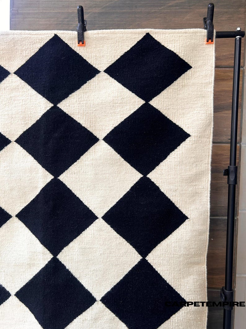 Minimalist wool rug featuring a timeless black and white diamond grid. The handwoven construction ensures quality and durability, while the 100% wool composition creates warmth underfoot. Perfect for Nordic, Japandi, or modern interiors with clean lines and natural tones.