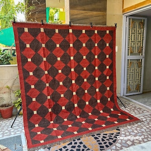 Flatweave red kilim rug featuring tribal-inspired motifs and earth-toned borders, created by skilled artisans using a wool and jute blend. The natural, breathable texture complements warm interiors and provides a cozy, cultural feel that works beautifully in spaces ranging from modern lofts to traditional homes.