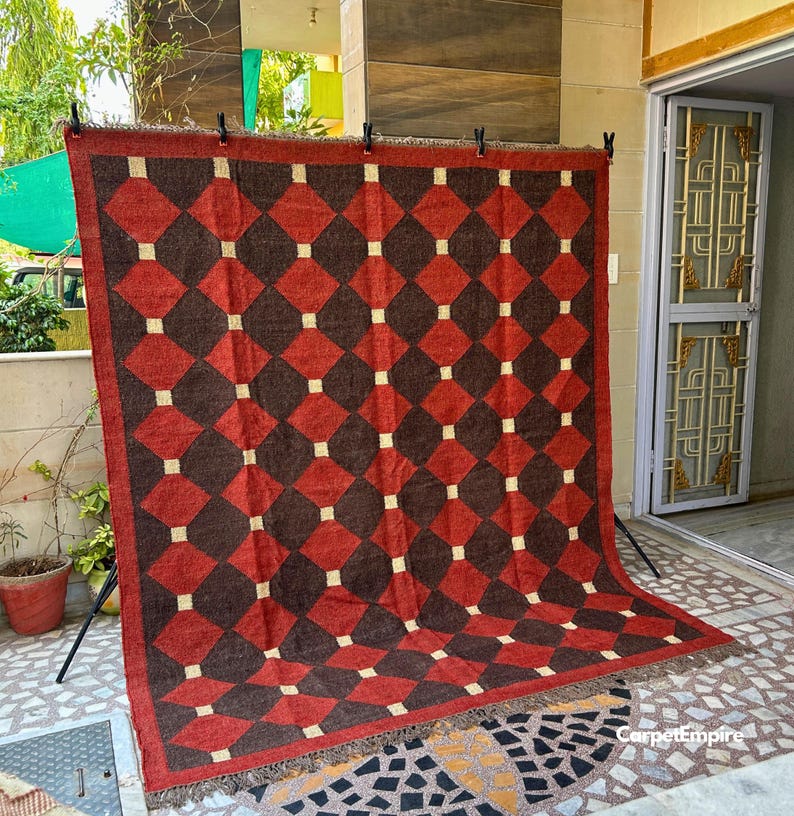 Flatweave red kilim rug featuring tribal-inspired motifs and earth-toned borders, created by skilled artisans using a wool and jute blend. The natural, breathable texture complements warm interiors and provides a cozy, cultural feel that works beautifully in spaces ranging from modern lofts to traditional homes.