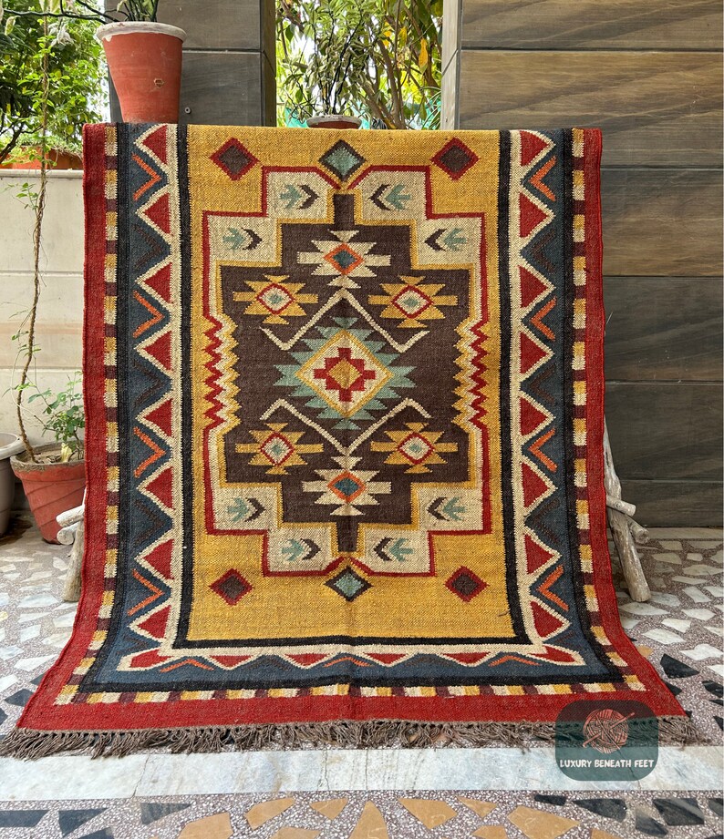 May include: A colorful, geometric patterned rug with a yellow background, red, blue, and brown accents. The rug has a fringe border and is made of wool.
