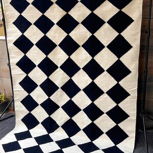 Black and white checkered wool area rug crafted with a geometric diamond pattern. This handwoven rug adds texture and visual balance to any modern room, combining luxurious wool softness with artisan craftsmanship. Ideal for flatweave lovers and sustainable home design.
