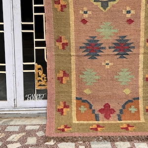 May include: A pink, green, blue, and orange patterned rug with a fringe border. The rug is made of woven jute and has a geometric design.