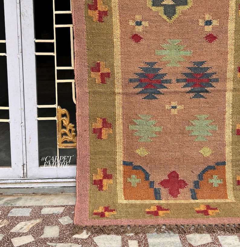 May include: A pink, green, blue, and orange patterned rug with a fringe border. The rug is made of woven jute and has a geometric design.