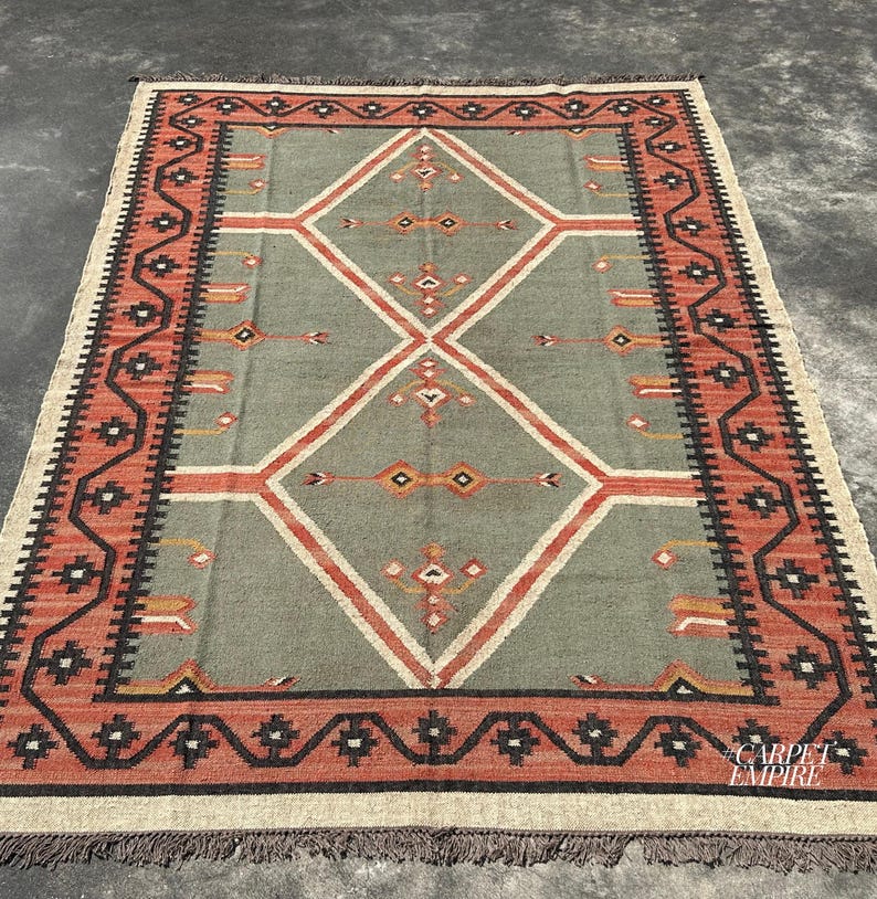 Sage green and terracotta wool jute kilim area rug with stacked diamond medallions and tribal motifs. Ornate terracotta border with zigzag wave. Handwoven. Custom sizes.