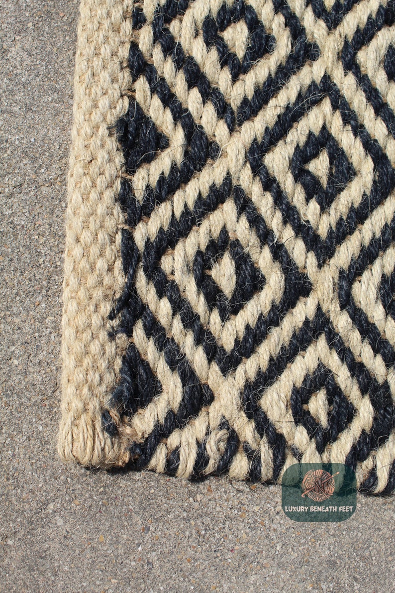 May include: Close-up of a black and natural jute rug with a geometric pattern. The rug has a woven texture and a frayed edge.