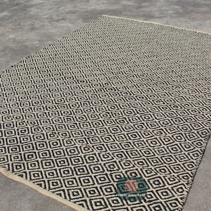 May include: Black and white geometric patterned rug with a diamond design. The rug is made of natural fibres and has a woven texture.