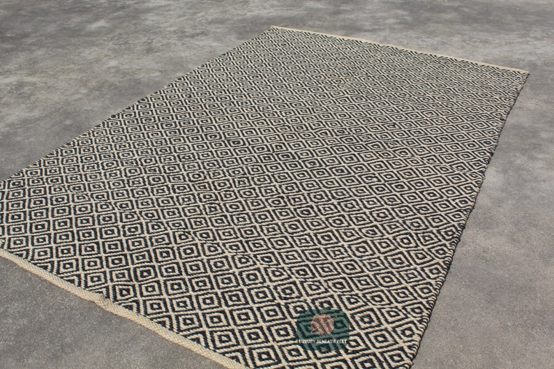 May include: Black and white geometric patterned rug with a diamond design. The rug is made of natural fibres and has a woven texture.