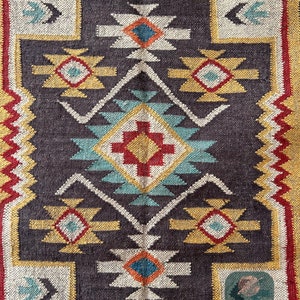 May include: A colorful rug with a geometric pattern in shades of red, yellow, blue, and white. The rug has a dark brown background and a white border.