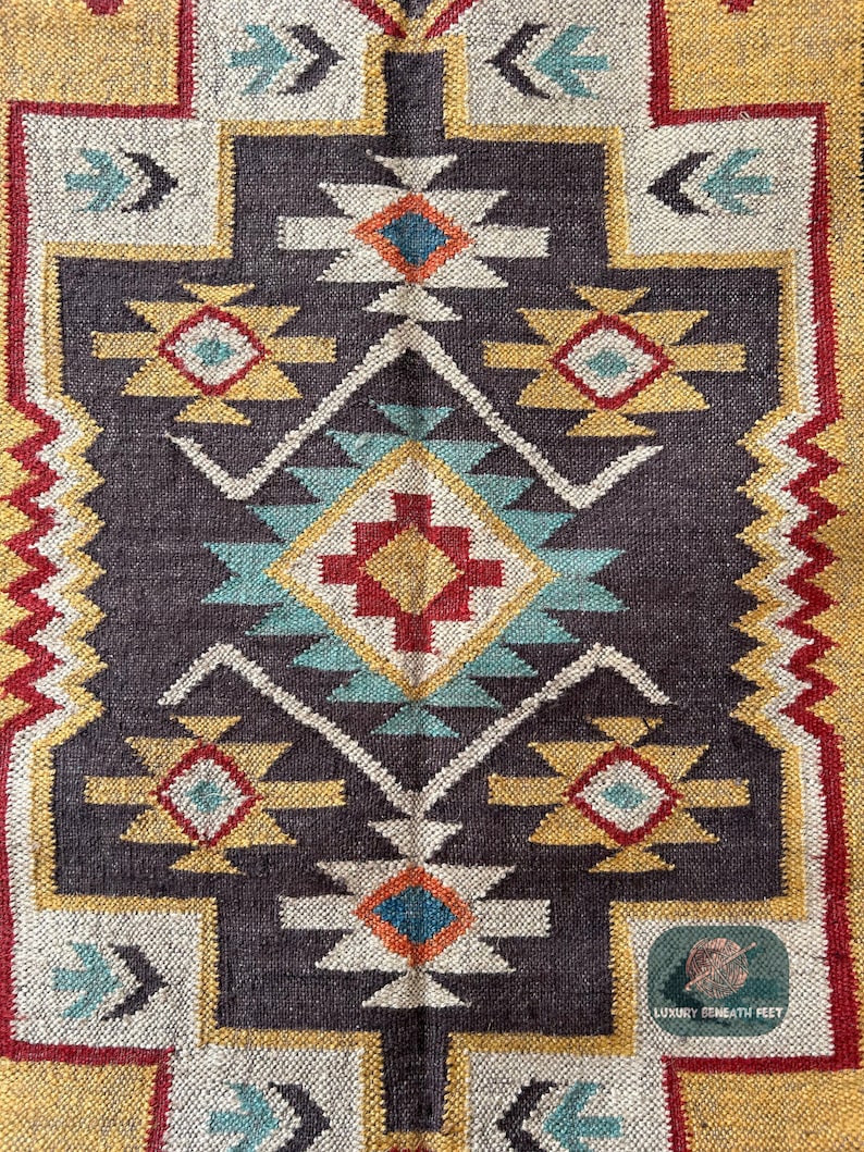 May include: A colorful rug with a geometric pattern in shades of red, yellow, blue, and white. The rug has a dark brown background and a white border.