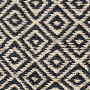 May include: Close-up of a woven rug with a geometric pattern in black and natural beige. The pattern is made up of repeating diamond shapes.