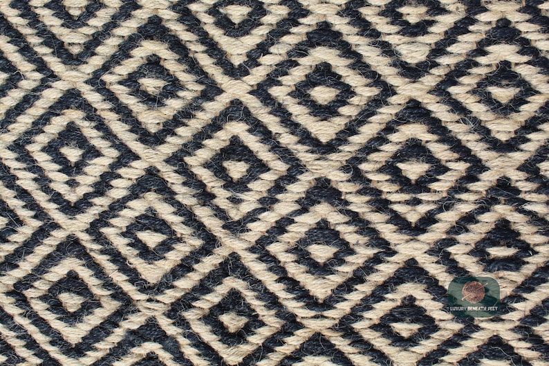 May include: Close-up of a woven rug with a geometric pattern in black and natural beige. The pattern is made up of repeating diamond shapes.