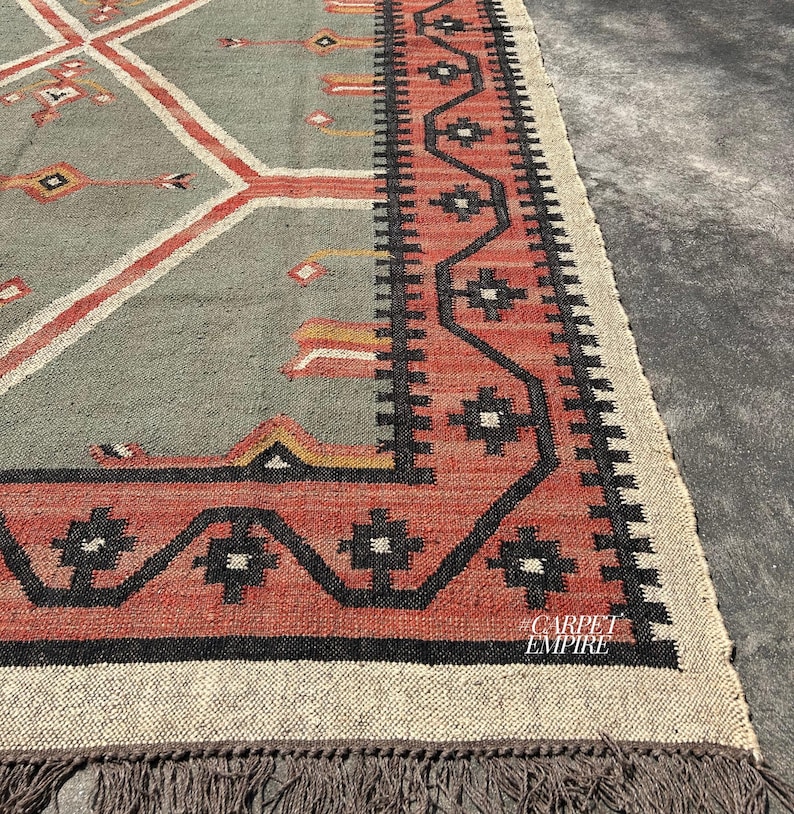 Green kilim rug with diamond medallions in terracotta and cream on sage field. Tribal cross compass motifs and ornate border. Wool jute handwoven flatweave. Custom size.