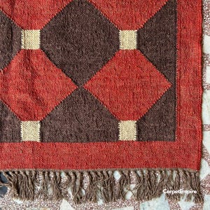 Handmade Indian kilim rug in deep red, accented with mustard, cream, and brown tones. The intricate flatweave features classic tribal shapes and sustainable natural fibers, offering both durability and style. Perfect for layering in modern boho living rooms, reading corners, or warm-toned bedrooms for a grounded, organic look.