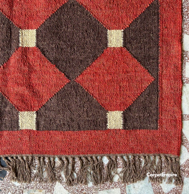 Handmade Indian kilim rug in deep red, accented with mustard, cream, and brown tones. The intricate flatweave features classic tribal shapes and sustainable natural fibers, offering both durability and style. Perfect for layering in modern boho living rooms, reading corners, or warm-toned bedrooms for a grounded, organic look.
