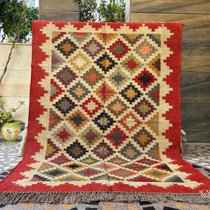 May include: A red, beige, and brown patterned rug with a geometric design. The rug has a fringe border and the text "#CARPETEMPIRE" in the bottom right corner.