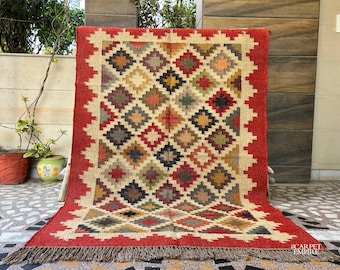 Può includere: Un tappeto rosso, beige e marrone con un design geometrico. Il tappeto ha un bordo a frangia e il testo "#CARPETEMPIRE" nell'angolo in basso a destra.