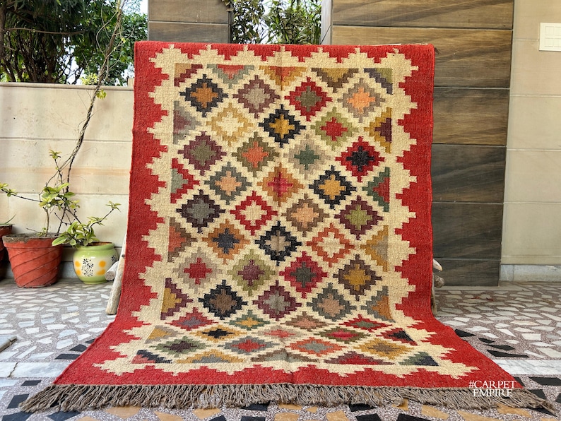 May include: A red, beige, and brown patterned rug with a geometric design. The rug has a fringe border and the text "#CARPETEMPIRE" in the bottom right corner.