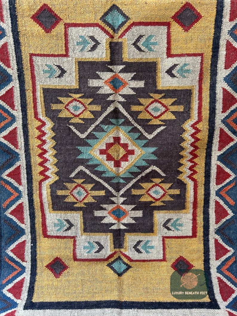 May include: A colorful rug with a geometric pattern in shades of red, blue, yellow, and white. The rug has a dark brown background and a border of blue, red, and white triangles.
