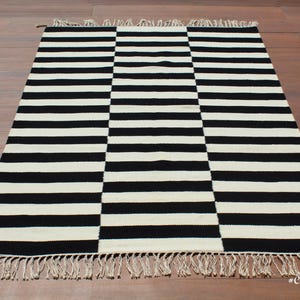 Elevate your interior with this handmade black and white wool rug, a versatile piece that complements modern, rustic, and farmhouse decor. Its geometric striped pattern adds a dynamic visual element, while the soft wool fibers provide a plush, comfortable feel. This durable rug is perfect for high-traffic areas, making it an excellent choice for entryways and hallways.