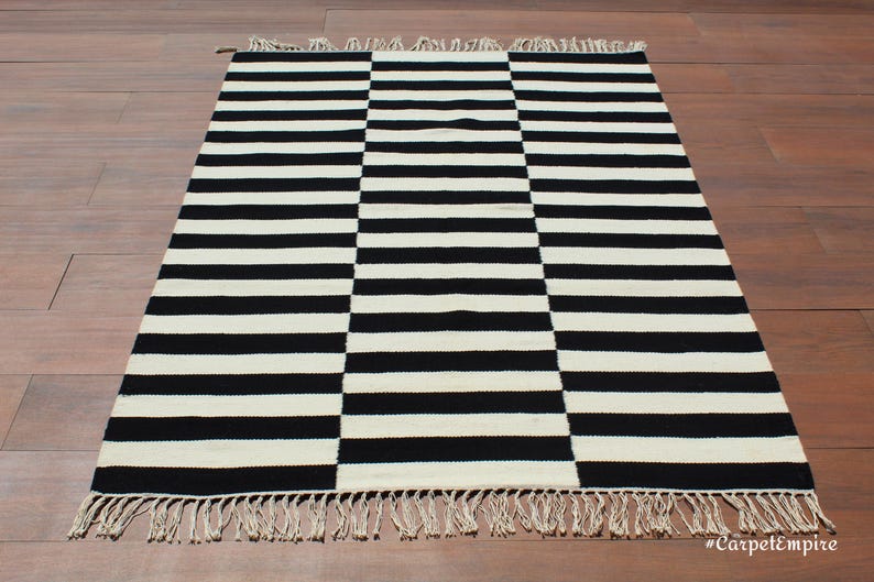 Elevate your interior with this handmade black and white wool rug, a versatile piece that complements modern, rustic, and farmhouse decor. Its geometric striped pattern adds a dynamic visual element, while the soft wool fibers provide a plush, comfortable feel. This durable rug is perfect for high-traffic areas, making it an excellent choice for entryways and hallways.