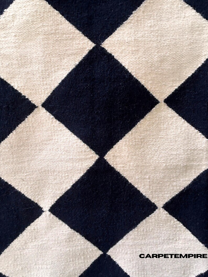 Modern geometric wool rug with black and white diamond check pattern. The handcrafted flatweave texture gives a clean and minimalist look, ideal for Scandinavian or neutral home decor. Made from 100% wool for comfort and durability, this rug complements living rooms, bedrooms, and minimalist office spaces.