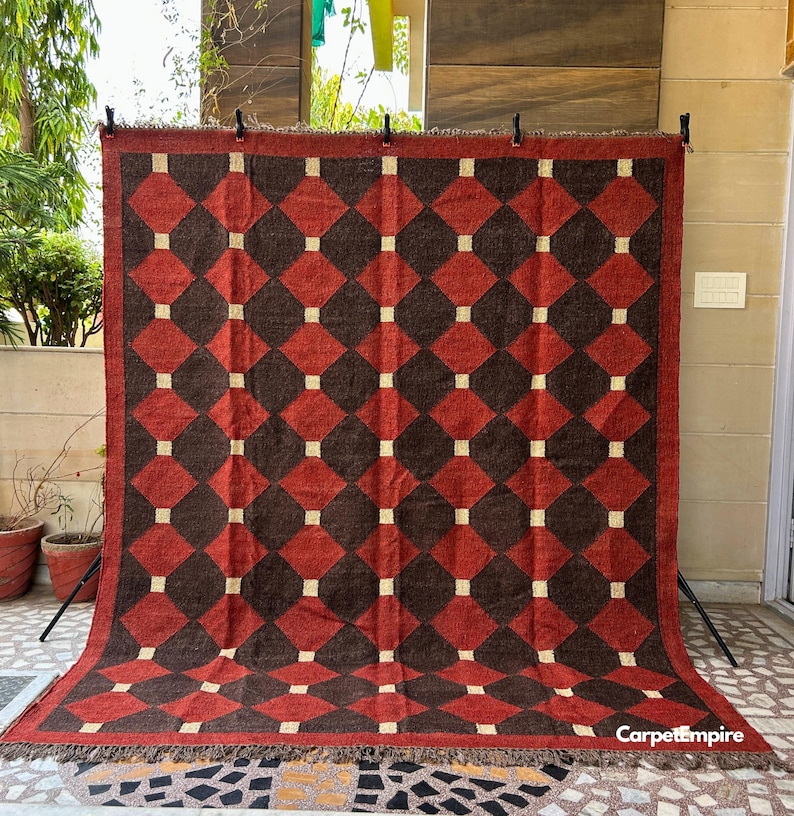 Artisan flatweave kilim rug with a geometric tribal design in earthy red and ochre tones. Made from a high-quality wool and jute blend, this eco-friendly rug is handmade using time-honored dhurrie weaving methods. Its rich colors and low-pile texture make it a versatile choice for hallways, bedrooms, or small sitting areas.