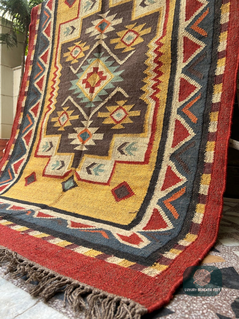 May include: A hand-woven rug with a geometric pattern in shades of red, yellow, blue, and brown. The rug has a fringe border and is made of natural fibers.