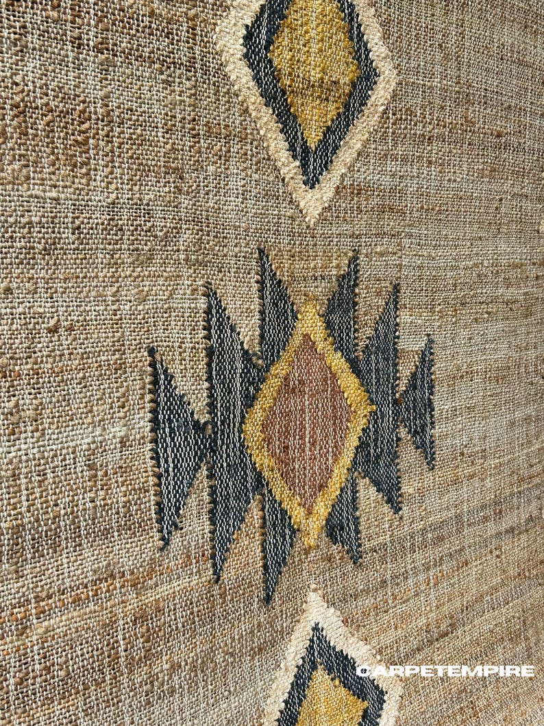 Flatwoven jute kilim rug with warm beige ground, soft cream motif details, and a defining dark border in purplish‑black. Crafted from natural jute fibers, this rug adds natural texture underfoot and a handcrafted aesthetic. Ideal for rooms with light wood floors, linen textiles, or neutral palettes, giving depth through geometric pattern and natural material without bold or bright tones.