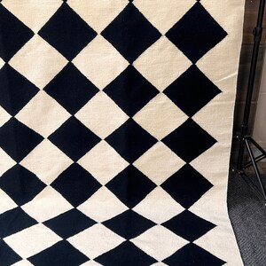 Handmade black and white geometric wool rug featuring a diamond checkered pattern. The flatweave design offers a soft yet sturdy texture that enhances modern and minimalist spaces. Perfect for Scandinavian, boho, or Japandi interiors seeking understated elegance.