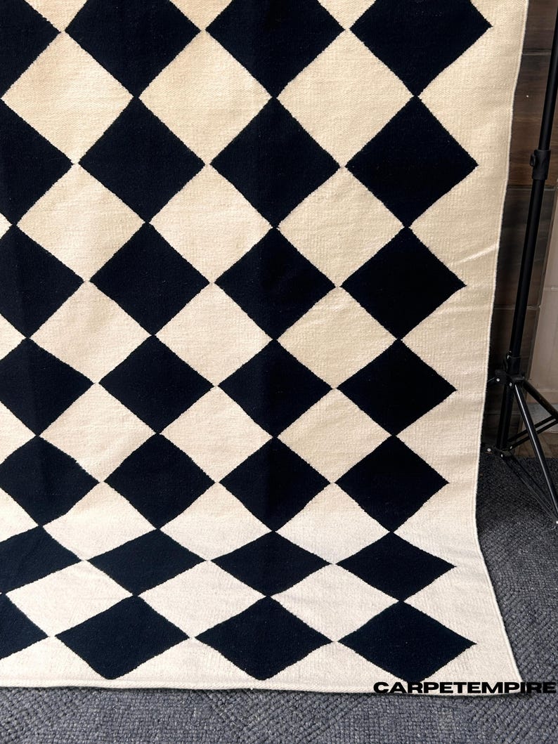 Handmade black and white geometric wool rug featuring a diamond checkered pattern. The flatweave design offers a soft yet sturdy texture that enhances modern and minimalist spaces. Perfect for Scandinavian, boho, or Japandi interiors seeking understated elegance.