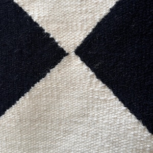 Handmade black and white check wool rug with geometric diamond patterns. The soft wool fibers and flatweave texture create a cozy yet clean finish, ideal for living rooms or bedrooms styled in Scandinavian or modern decor themes.