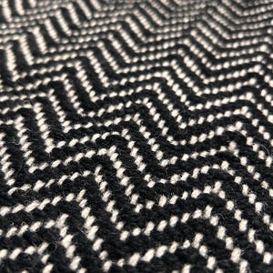 May include: Close-up of a black and white woven fabric featuring a chevron pattern. The fabric has a textured appearance with a repeating zigzag design. The text "CARPETEMPIRE" is visible in the lower right corner.