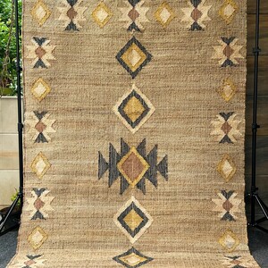 Beige jute area rug with cream kilim pattern and contrasting dark border in purplish‑black, handwoven in a flatweave weave using natural fibers. This rug brings warmth and organic texture to minimalist, farmhouse, or Moroccan‑inspired interiors. Low pile makes it easier to vacuum and safe for placing furniture, perfect for those wanting natural elegance without heavy color or high shine.