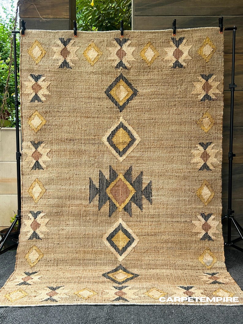 Beige jute area rug with cream kilim pattern and contrasting dark border in purplish‑black, handwoven in a flatweave weave using natural fibers. This rug brings warmth and organic texture to minimalist, farmhouse, or Moroccan‑inspired interiors. Low pile makes it easier to vacuum and safe for placing furniture, perfect for those wanting natural elegance without heavy color or high shine.