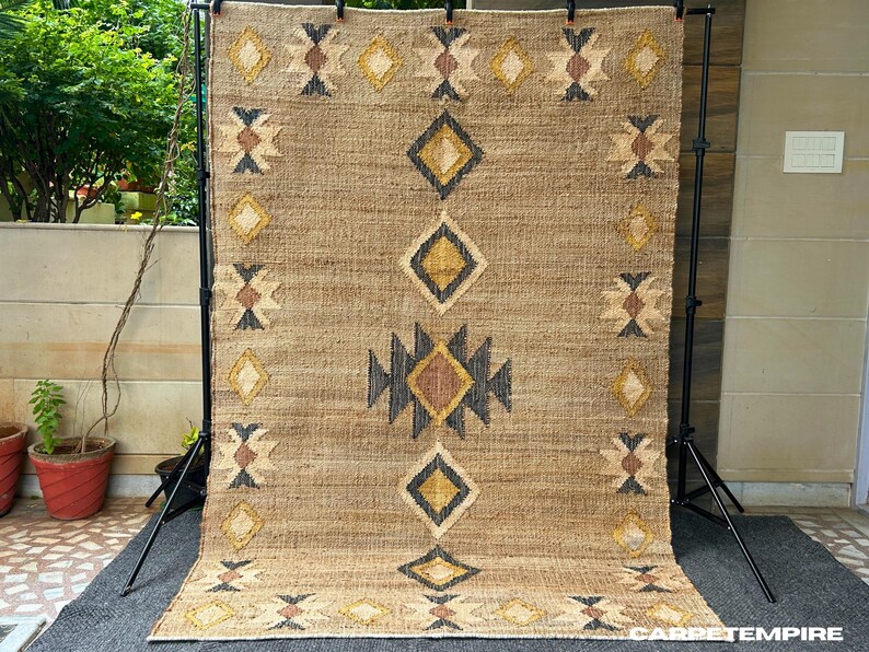 Cream motif kilim design set against a beige jute field with subtle dark border, handwoven with natural fibers for texture and durability. Flatweave jute rug brings organic warmth and structure, ideal for layering over wood floors or pairing with simple furniture. Muted tones and simple pattern make this rug well suited for quiet spaces that need anchor without noise.