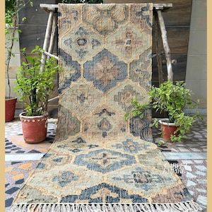 May include: A beige and blue patterned jute rug with fringe. The rug has a geometric design with a central diamond shape.